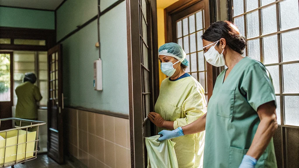 Nurses in gloves, gown, mask and cap preparing to enter an isolation room, illustrating standard and transmission-based precautions