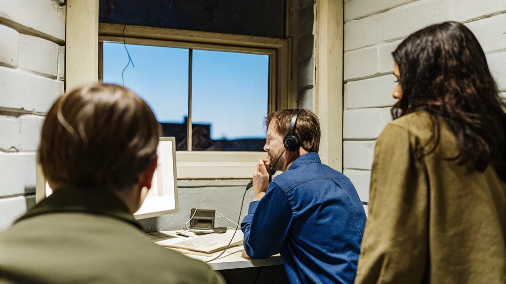 Engineers in a sunlit control room evaluate a speech recognition system, one speaking into a headset while colleagues look on.