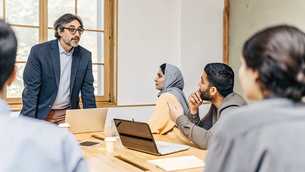 Manager speaking with calm confidence to an attentive team around a meeting table